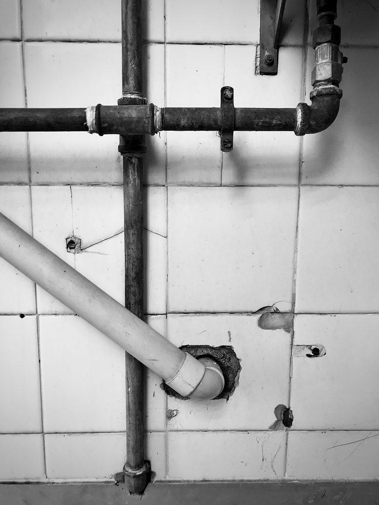 A black and white photograph of criss-crossing pipes emerging from a tiled wall