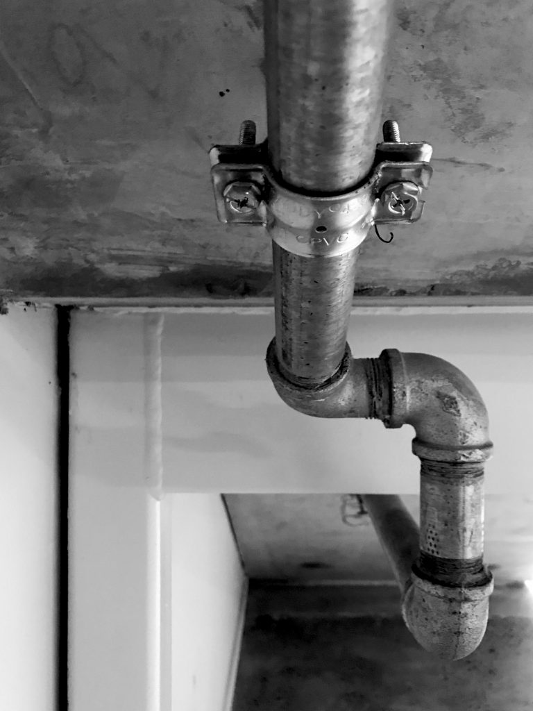 A black and white photograph of a pipe emerging from a cavity in a wall