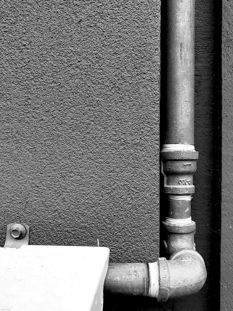 A black and white photograph of a concrete wall and drain pipe