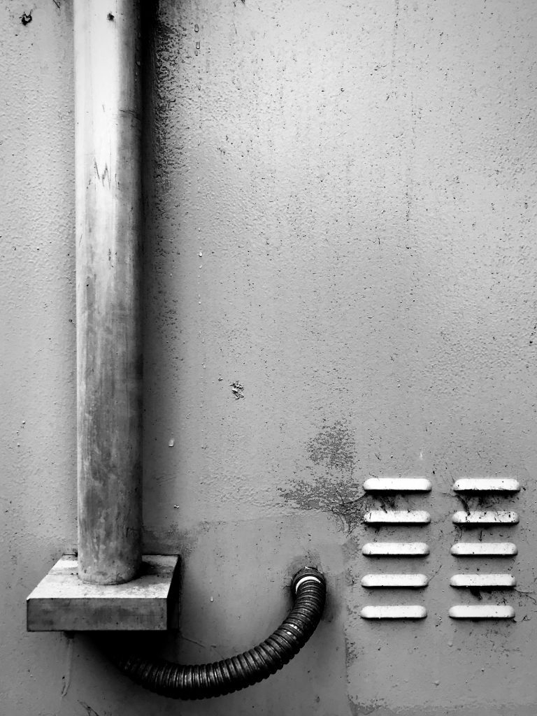 A black and white photograph of a single drain pipe and vents