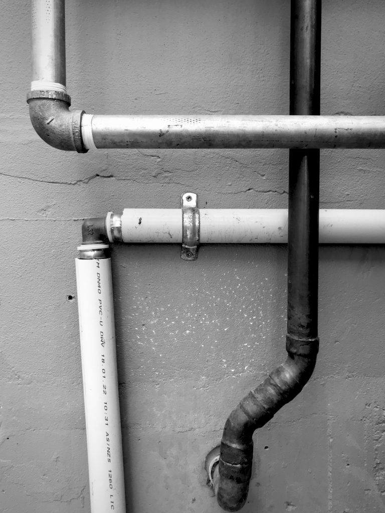 A black and white photograph of a group of pipes creating a grid effect against a wall.