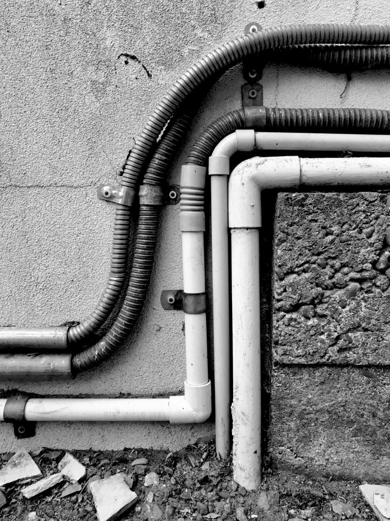 A black and white photograph of a group of pipes running across a concrete surface.
