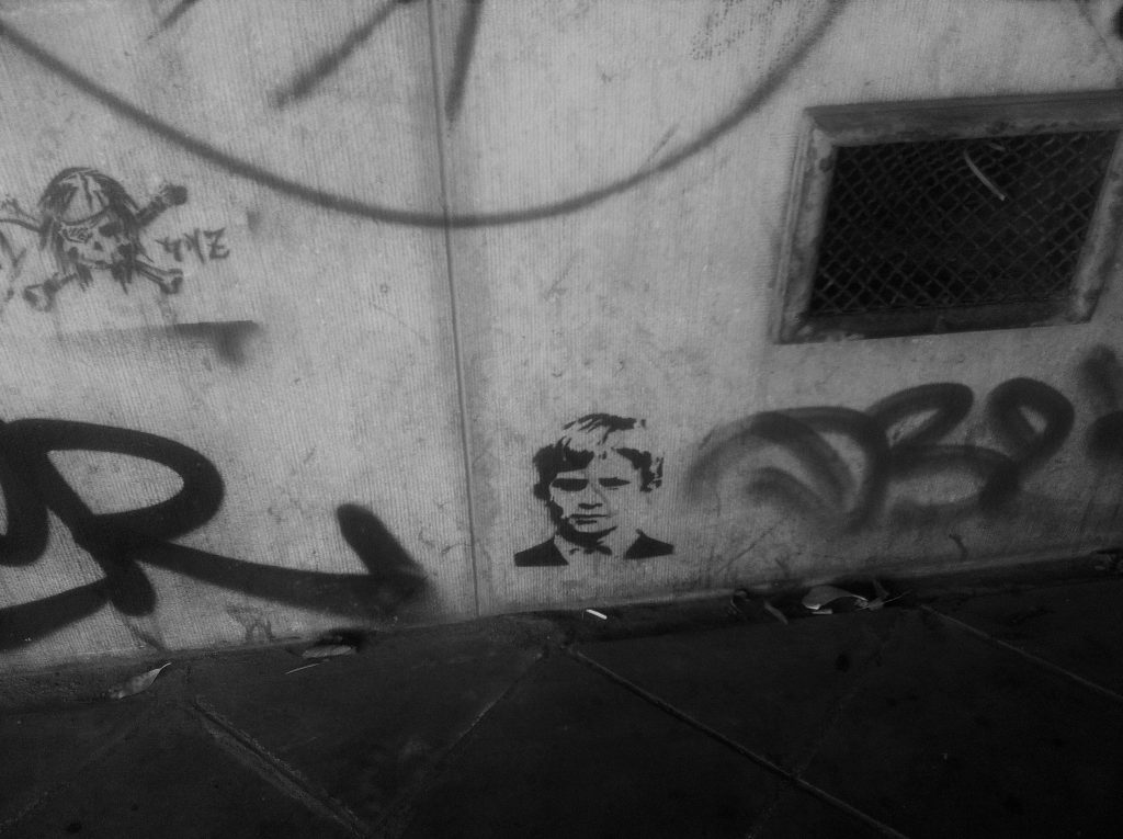  A graffitied wall featuring stencils, one of which is a skull and cross bones, the other a portrait of a young boy