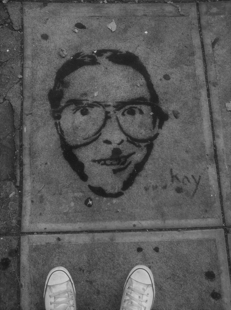 A stencil of a face with large glasses on a footpath in San Francisco