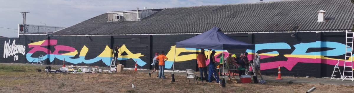 Members of the New Brighton community helpe the Fiksate crew and the NBOAF organisers paint the Welcome to Orua Paeroa mural.