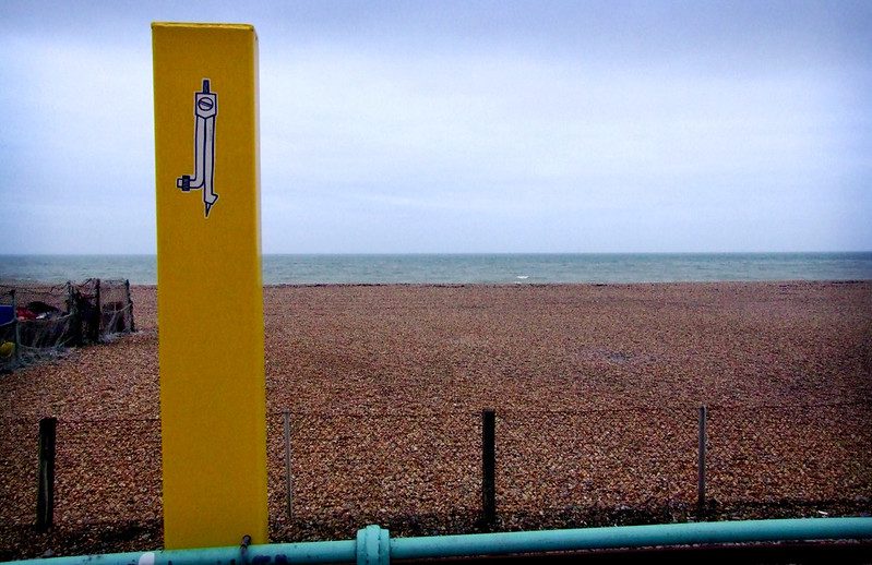 A small Teeth Like Screwdrivers compass sticker on a yellow pole on the beach, Brighton, United Kingdom (photo credit: Butterstotch)